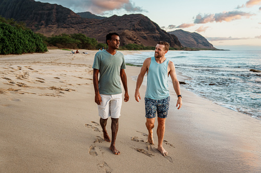 An Indian man and Caucasian man enjoy good conversation and a relaxing walk along the beach in Hawaii.