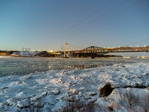 View of Quebec city bridges, the old bridge and the Pierre-Laporte bridge during dusk of winter with ice moving on the St. Lawrence river