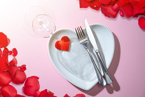 Overhead shot of white dinner plate with two silver heart shaped rings and cutlery on white background.