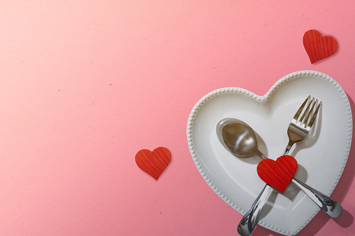 Heart plate with silverware of spoon and fork with a red heart over a pink background. Romantic dinner Valentine's Day concept