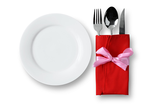 White plate with silverware of fork, knife, and spoon in red napkin isolated over a white background. Romantic dinner Valentine's Day concept