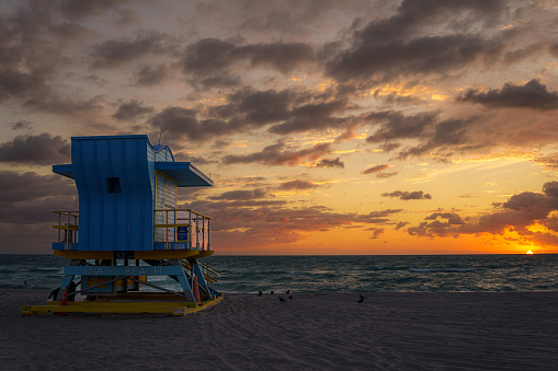 View of the beautiful sun setting behind a blue lifeguard tower on the beach in the Winter in Florida.