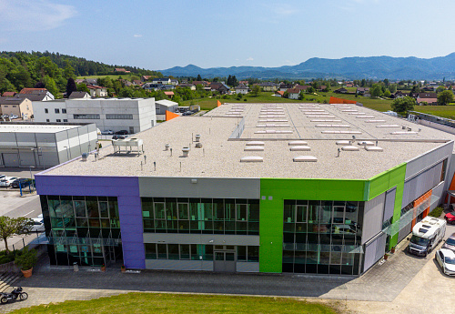 Aerial view of a modern industrial building with colorful facade, surrounded by cars and greenery, under a clear sky.