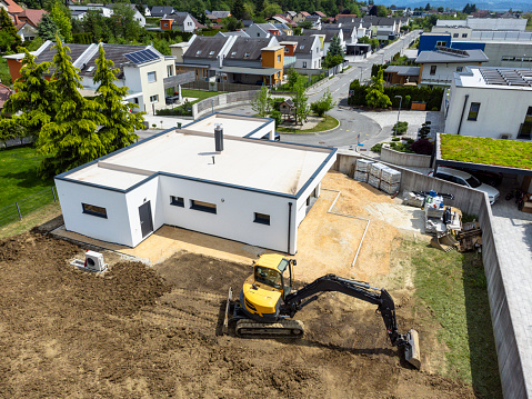 Aerial view of a modern house with a backyard under construction, featuring an excavator on a sunny day.