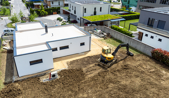 Aerial view of a modern house with a backyard under construction, featuring an excavator on a sunny day.