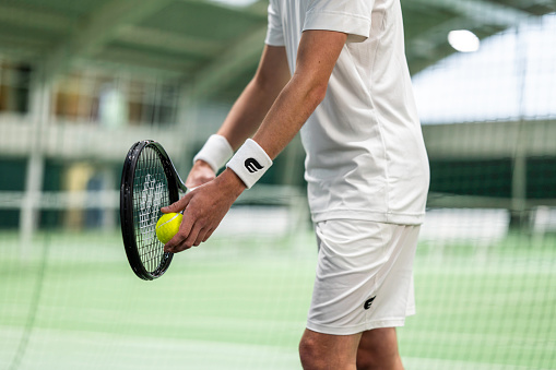 Male tennis player holding racket while preparing to serve ball, med section