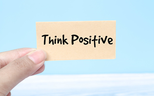Woman holding paper spelling words Think Positive on blue background. Torn piece of paper with the words Think Positive in the woman's hand.Think Optimistic Attitude Mindset Concept