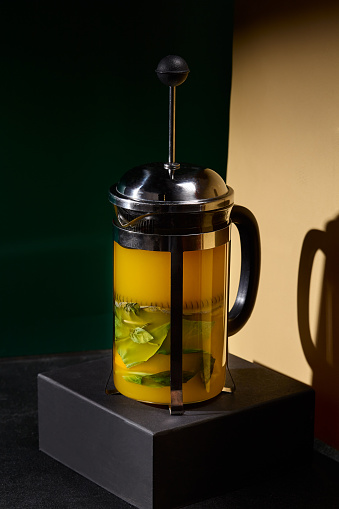 A bespoke tea blend showcased in a translucent French press, accentuated by zesty orange slices and cool mint leaves, juxtaposed against a minimalist black and beige color-block setting.