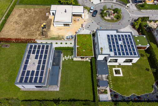 Aerial view of modern houses with solar panels on roofs and one of the houses being built, sustainable energy concept.