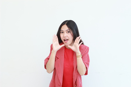 portrait of beautiful asian woman wearing red outfit with whispering gesture isolated on white background.