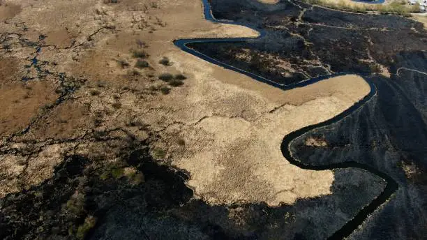 Aerial View of a Meandering River Through a Burnt Grassland After Fire. High quality 4k footage