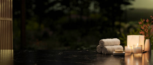 A copy space on a black marble table featuring towels, candles, a soap, and a lamp in a dark room.