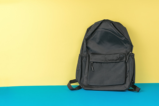 Classic black backpack on a yellow and blue background. Universal shoulder bag.
