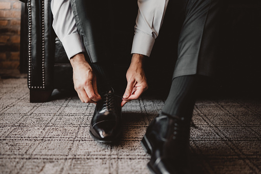 Groom putting on black dress shoes at his wedding