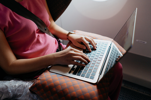 Female business entrepreneur traveling in business class and working with laptop on an airplane. Business travel and vacation concept.