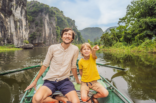 Dad and son tourists in boat on the lake Tam Coc, Ninh Binh, Viet nam. It's is UNESCO World Heritage Site, renowned for its boat cave tours. It's Halong Bay on land of Vietnam. Vietnam reopens borders after quarantine Coronovirus COVID 19.