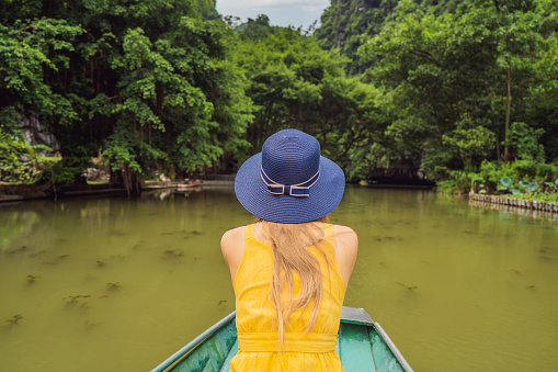 Woman tourist in boat on the lake Tam Coc, Ninh Binh, Viet nam. It's is UNESCO World Heritage Site, renowned for its boat cave tours. It's Halong Bay on land of Vietnam. Vietnam reopens borders after quarantine Coronovirus COVID 19.