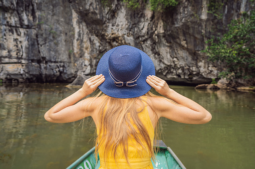 Woman tourist in boat on the lake Tam Coc, Ninh Binh, Viet nam. It's is UNESCO World Heritage Site, renowned for its boat cave tours. It's Halong Bay on land of Vietnam. Vietnam reopens borders after quarantine Coronovirus COVID 19.