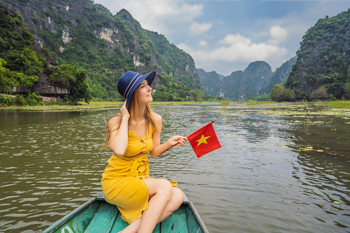 Woman tourist in boat on the lake Tam Coc, Ninh Binh, Viet nam. It's is UNESCO World Heritage Site, renowned for its boat cave tours. It's Halong Bay on land of Vietnam. Vietnam reopens borders after quarantine Coronovirus COVID 19.