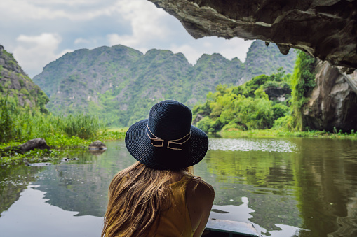 Woman tourist in boat on the lake Tam Coc, Ninh Binh, Viet nam. It's is UNESCO World Heritage Site, renowned for its boat cave tours. It's Halong Bay on land of Vietnam. Vietnam reopens borders after quarantine Coronovirus COVID 19.