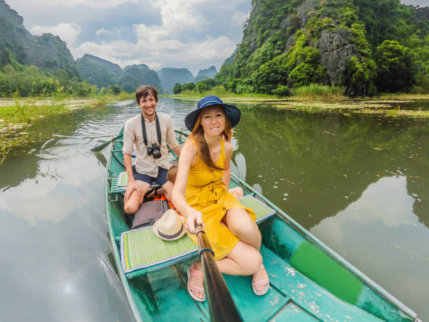 Happy family tourists in boat on the lake Tam Coc, Ninh Binh, Viet nam. It's is UNESCO World Heritage Site, renowned for its boat cave tours. It's Halong Bay on land of Vietnam. Vietnam reopens borders after quarantine Coronovirus COVID 19. turistas familiares felices en bote en el lago tam coc, ninh binh, vietnam. es patrimonio de la humanidad de la unesco, famoso por sus recorridos en barco por las cuevas. es la bahía de halong, en tierra de vietnam. vietnam reabre fronteras tras cuarenten