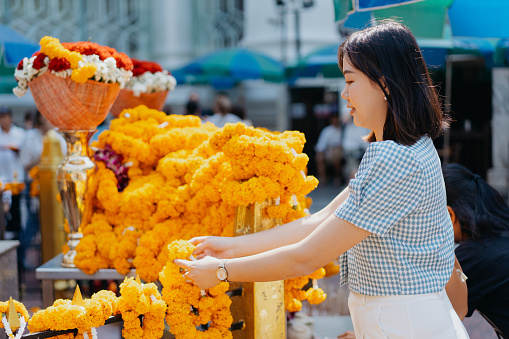 An Asian woman putting marigold on the shrine while praying to four faced Buddha at Erawan Shrine in Bangkok, Thailand