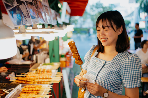 An Asian Chinese woman buying street food BBQ pork skewer \