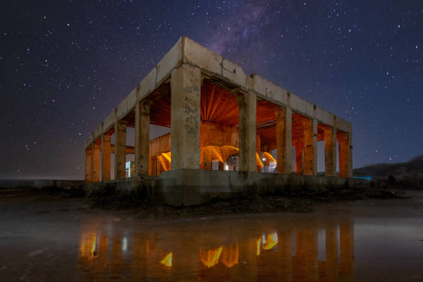 A night view of a coastal town with buildings and distant lights glowing over the horizon, blending with the dark sea.