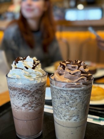 Stock photo showing close-up view of restaurant table setting with two glasses of Mocha Frappuccino with a cold caffeinated, blended drink made with ice, espresso, chocolate syrup, and milk, topped with whipped cream or chocolate flavoured squirty cream.