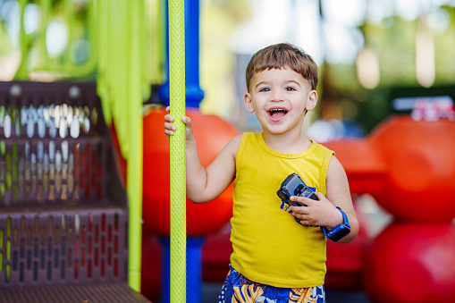 An adorable multiracial toddler boy of Puerto Rican descent smiles to the camera while playing on the playground of a public park in a Florida neighborhood.
