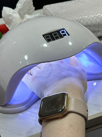 Stock photo showing close-up, elevated view of a woman drying her manicured painted nails design under a uv curing light.