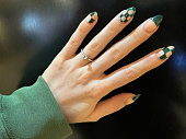 Image of unrecognisable woman showing left hand displaying engagement ring and nail art, fanned out fingers showing green checked pattern nail varnish manicure design, shiny, black background, focus on foreground