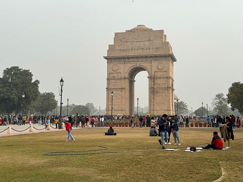 India Gate, New Delhi, India - January 6, 2024: Stock photo showing close-up view of crowds of tourists viewing the India Gate originally called the All India War Memorial in polluted foggy mist, from the surrounding India Gate lawns and park, New Delhi, India.