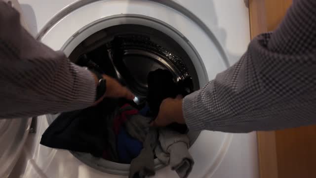 POV Man putting the clothes washer putting dirty clothes and taking out clean clothes, mechanical washing machine. Gender equality, responsibility, domestic chores, men, women, helping the family