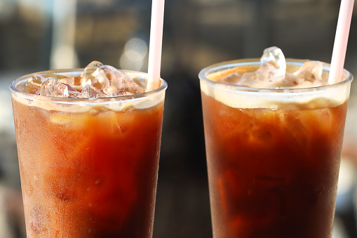 Stock photo showing close-up image of two drinks lined up on an al fresco wooden balcony railing. Pictured are iced coffees with ice cubes in drinking glass covered in condensation.