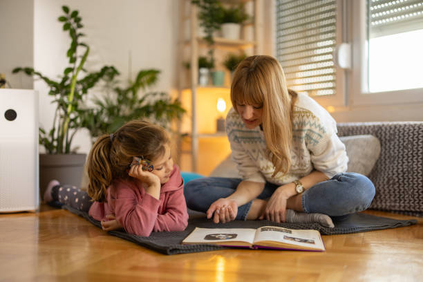 Mother and little daughter enjoying book together Devoted mother reading a book to her little daughter while sitting on floor at home parent and child reading stock pictures, royalty-free photos & images