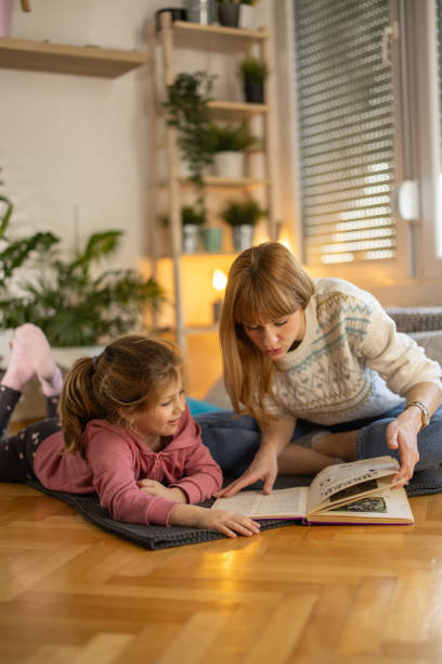 istock Mother and daughter reading book on the floor 1994401671