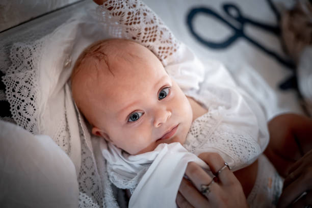 dressing up a small child in an Orthodox Christian church or temple during the sacrament of baptism in a baptismal outfit dressing up a small child in an Orthodox Christian church or temple during the sacrament of baptism in a baptismal outfit. pics of the godmother stock pictures, royalty-free photos & images