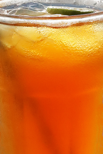 Stock photo showing close-up view of citrus orange mock cocktail with ice cubes and lime slice in drinking glass covered in condensation.