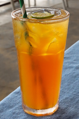 Stock photo showing close-up view of citrus orange mock cocktail with ice cubes and lime slice in drinking glass covered in condensation.