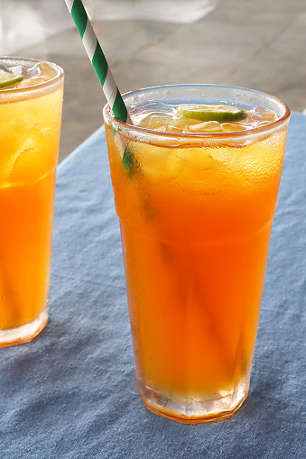Stock photo showing close-up view of two citrus orange mock cocktails with ice cubes and lime slice in drinking glass covered in condensation.