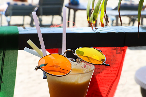 Stock photo showing close-up image of al fresco beach bar restaurant scene with a pair of tinted, mirrored sunglasses balanced on a glass of freshly squeezed orange juice.