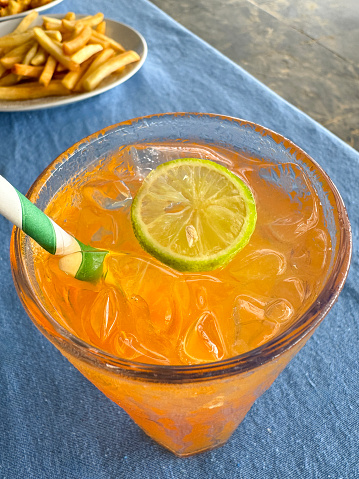 Stock photo showing close-up, elevated view of citrus orange mock cocktail with ice cubes and lime slice in drinking glass covered in condensation.