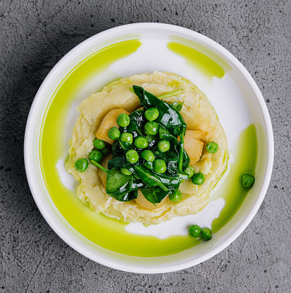 Mashed potato with butter, green peas, basil in a white bowl