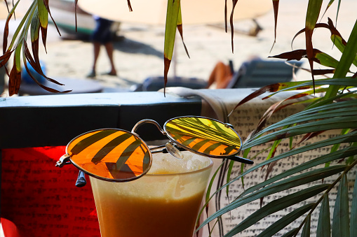 Stock photo showing close-up image of al fresco beach bar restaurant scene with a pair of tinted, mirrored sunglasses balanced on a glass of freshly squeezed orange juice.