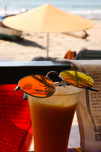 Stock photo showing close-up image of al fresco beach bar restaurant scene with a pair of tinted, mirrored sunglasses balanced on a glass of freshly squeezed orange juice.