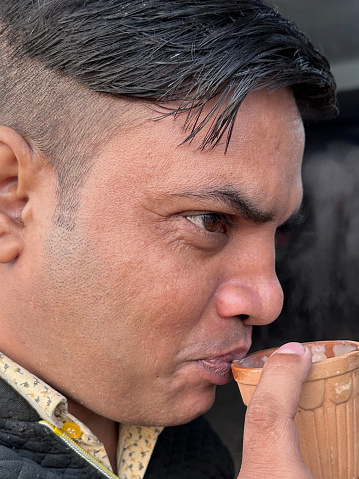 Stock photo showing close-up view of Indian man with botched new short back and sides haircut at street food stall sipping masala tea from a clay pot.