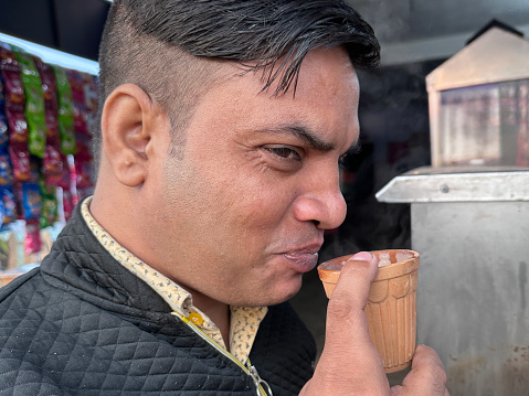 Stock photo showing close-up view of Indian man with botched new short back and sides haircut at street food stall sipping masala tea from a clay pot.