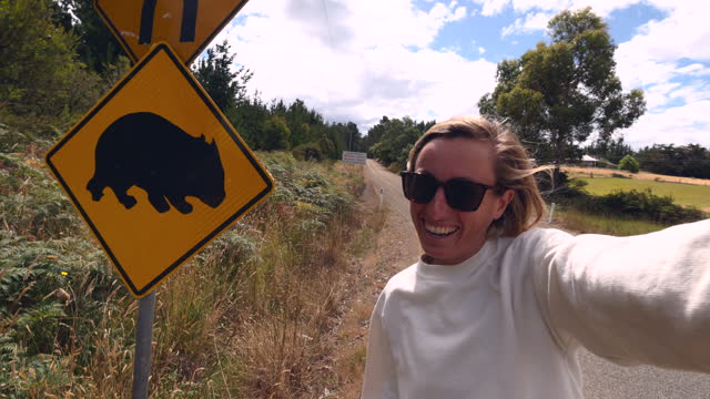 Slow Motion: Female traveller takes a selfie with warning wombat Australian road sign