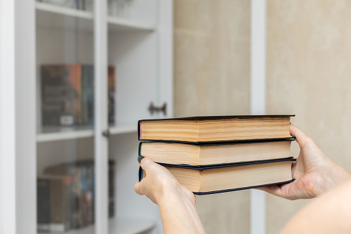 woman holding a book against the background of a bookcase. man takes out a book from a bookcase. man holding several paper books. some books. High quality photo